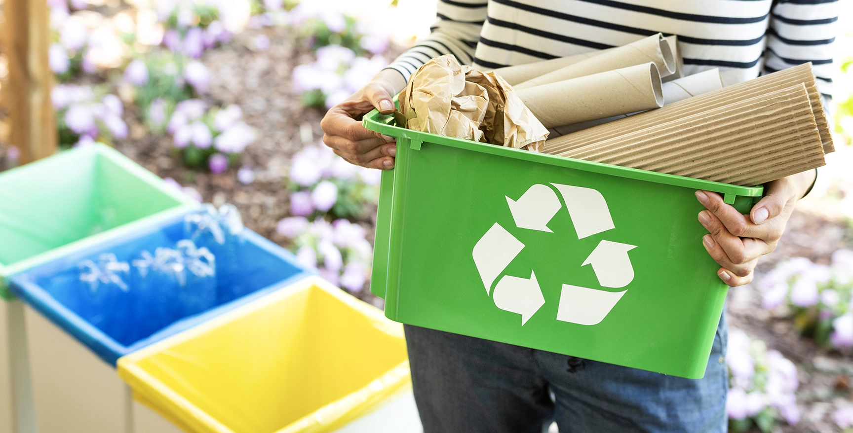 Grüner Korb mit einem Recyclingsymbol und Papieren, die von einer Frau gehalten werden